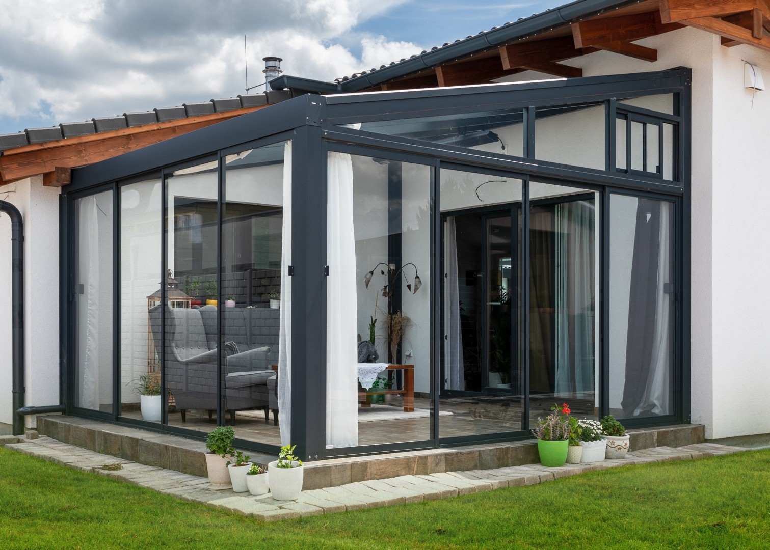 Moderná presklená hliníková pergola pripojená k domu s elegantným interiérovým nábytkom.